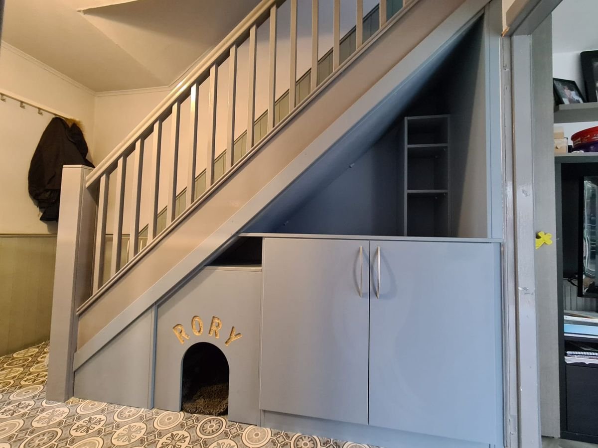 Grey under-stairs cupboards with a built-in dog bed and open shelving