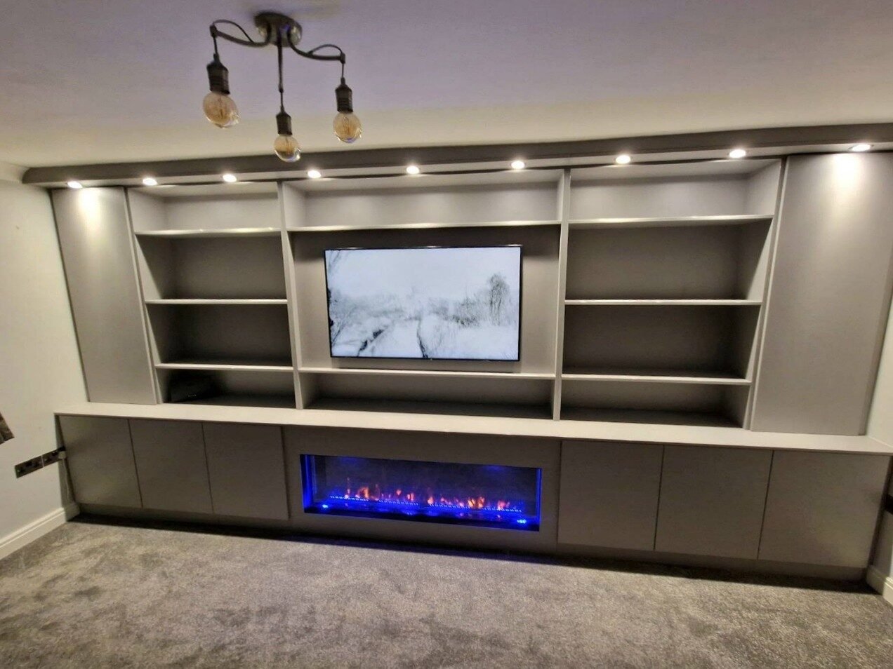 Media wall with electric fire and spotlights in the bulkhead above grey open shelving Media wall with electric fire and spotlights in the bulkhead above grey open shelving